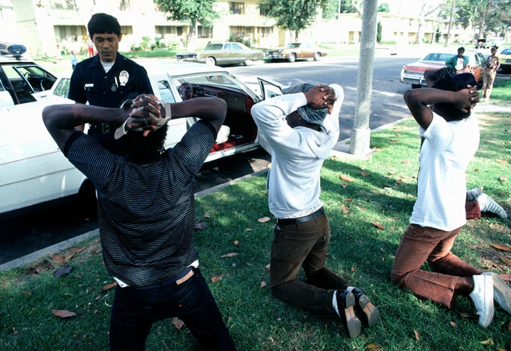 A "Crip" (left) dressed in blue, showing the Gang colors, is arrested by the Los Angeles Police Department anti-gang unit with two friends after stealing a Cadillac Car; a search turned up weapons and drugs. Oct. 16, 1984, Compton, South Central Los Angeles, California.