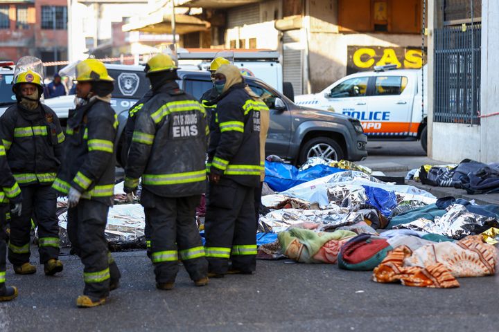 Πυροσβέστες στέκονται δίπλα σε καλυμμένα σώματα θυμάτων στον τόπο της φονικής πυρκαγιάς, στο Γιοχάνεσμπουργκ, της Νότιας Αφρικής (31/8/2023).