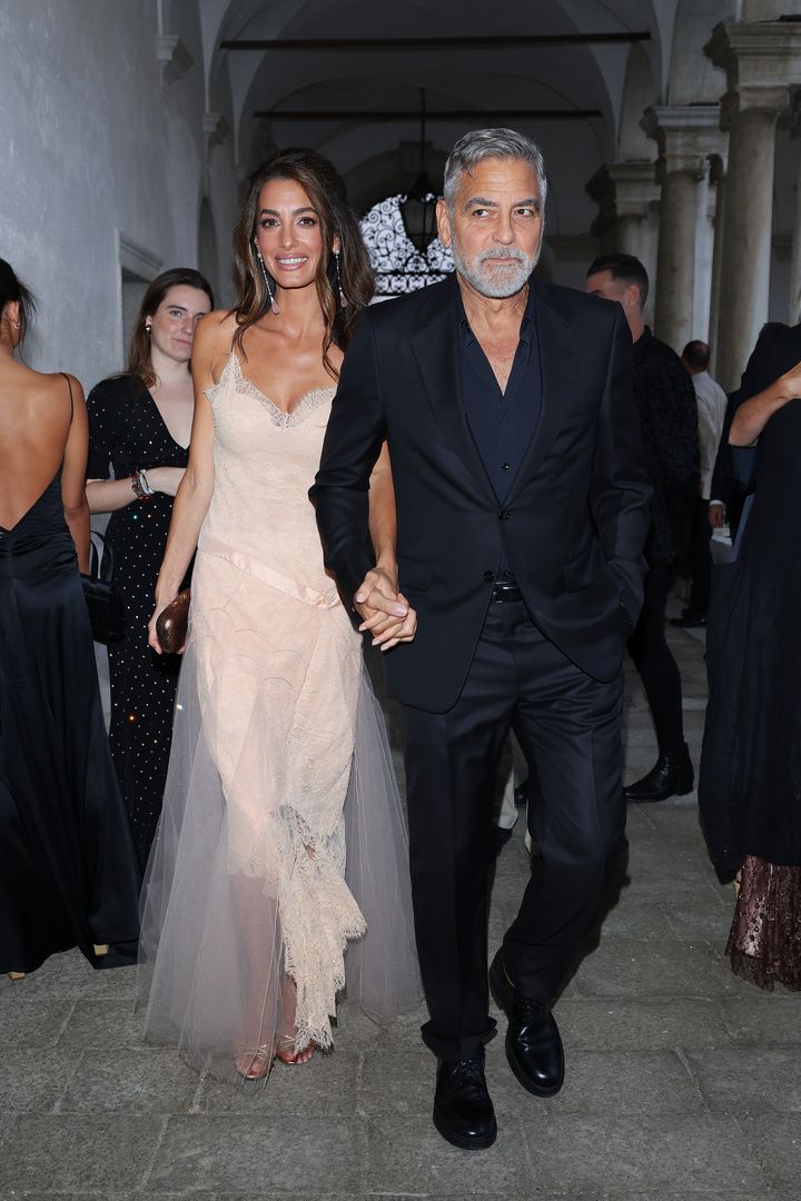Amal Clooney wears a flowing Christian Dior ensemble, crowned by her loosely waved brunet hair, as husband George escorts her in chic dark tones.