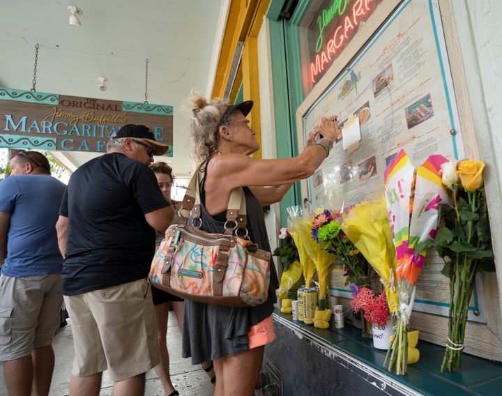 Susan Hudnall pins a condolence note about Jimmy Buffett's death to the front window of the Margaritaville Cafe in Key West, Florida on Saturday. Buffett, who popularized beach bum soft rock with the escapist Caribbean-flavored song "Margaritaville" and turned that celebration of loafing into a billion-dollar empire of restaurants, resorts and frozen concoctions, died Friday.