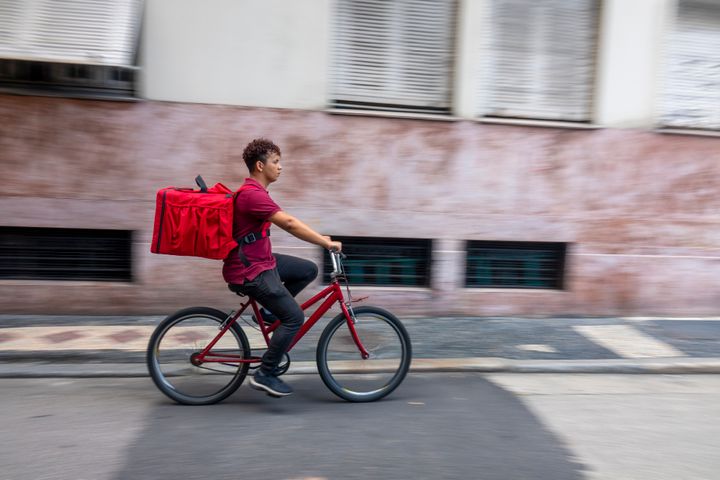 Young man pedals on the side of the street to make his delivery