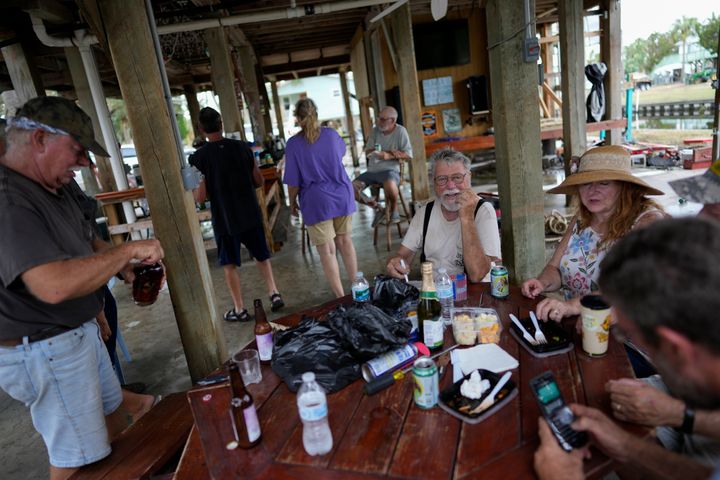 Sparky Abrandt, 77, center right, an electrician who moved to town five years ago, hosts friends on the lower level of his stilted home, in Horseshoe Beach, Fla., on Sept. 1, 2023, two days after the passage of Hurricane Idalia.