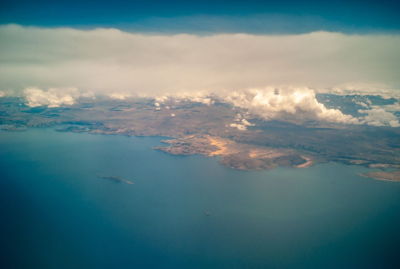 Αεροφωτογραφία του έρημου περιβάλλοντος της λίμνης Τιτικάκα και των μικροσκοπικών σπιτιών γύρω της με τα σύννεφα.