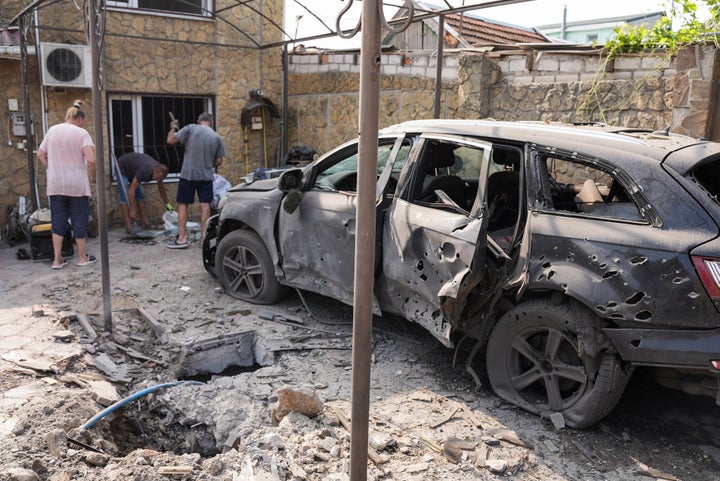 Locals clean up rubble near a damaged building and car after Russian shelling on Friday in Kherson, Ukraine.
