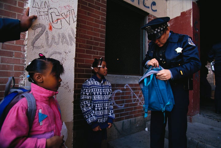 A police officer searches the bag of a young African American girl in the graffiti-covered Cabrini-Green housing project.