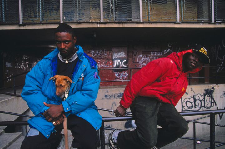 Two young men sit on a railing outside the Cabrini-Green housing project in Chicago, with one holding his pet dog inside his jacket to keep it warm.