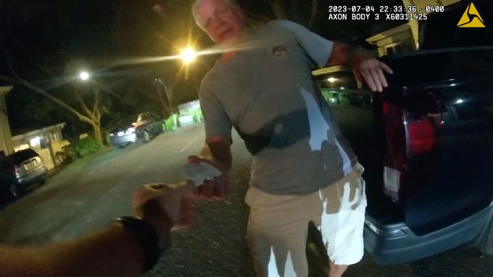 Joseph Ruddy is pictured handing his business card to a police officer on the evening of July 4 when police arrived at his house to investigate a hit-and-run.