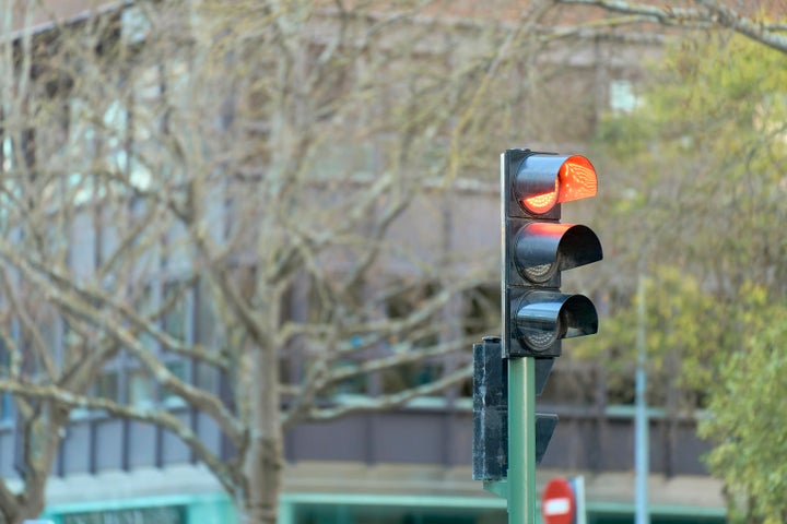 Red traffic light on at street intersection, leafless trees and buildings in the background.