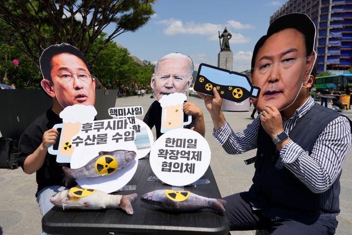 Protesters — wearing masks of political leaders from Japan, the U.S., and South Korea — are pictured during a rally denouncing a summit between the countries, in Seoul, South Korea, on May 19. They oppose the nations' military alliance and the release of treated radioactive water from a Fukushima nuclear power plant. The text reads, "Imported marine products from Fukushima."