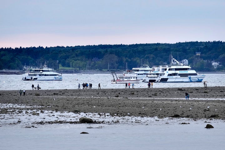 Visitors walk along a sandbar at low tide before Hurricane Lee, Friday, Sept. 15, 2023, in Bar Harbor, Maine.  Tour boats that normally offer whale- and puffin-watching excursions have been moved to safer anchorages in the background.  (AP Photo/Robert F. Bukaty)