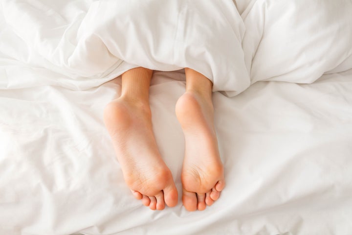 Boy's bare feet peeking out from a blanket on a bed with a white linen