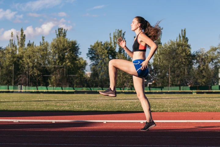 A sporty woman warming up on an athletics track before running.