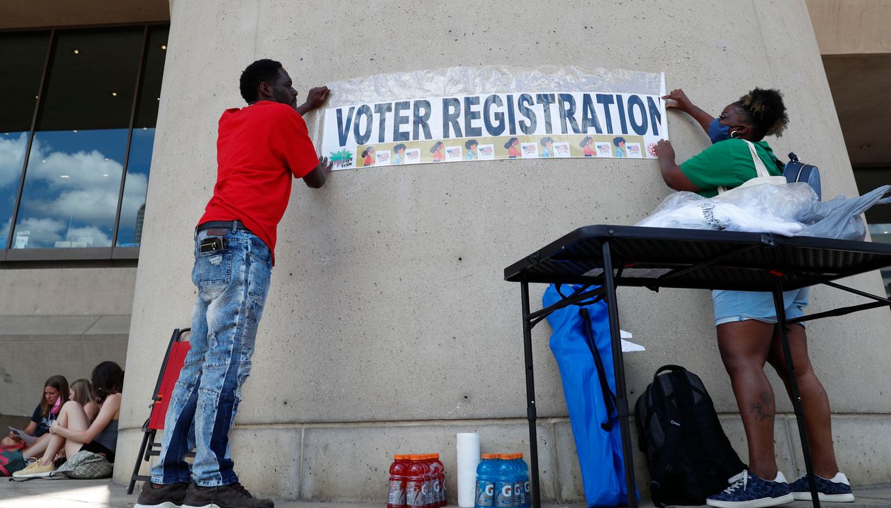 Aetry Jones, left, and Caerry Rigbon tape up a voter registration sign on Dallas City Hall before a Juneteenth 2020 celebration in Dallas on June 19, 2020.