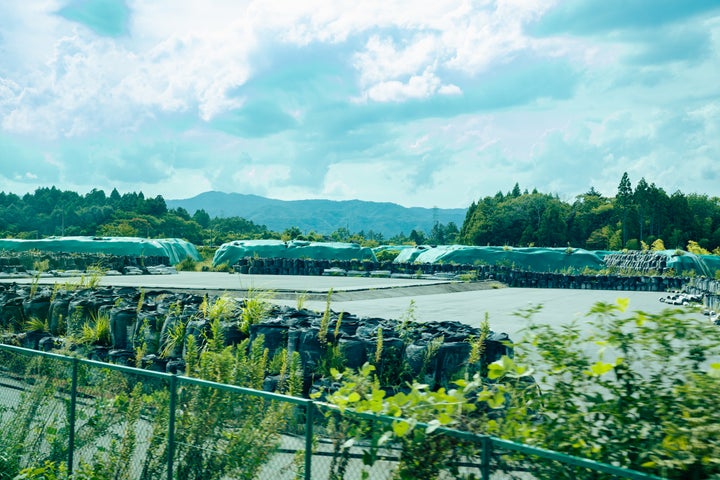 山積みにされたフレコンバッグの奥に、遮水シートで覆われた除去土壌が配置されている