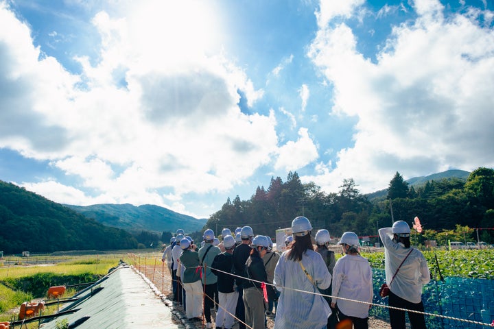 実証実験場を見学する参加者たち。飯舘村長泥地区環境再生事業エリア職員の説明に耳を傾けている