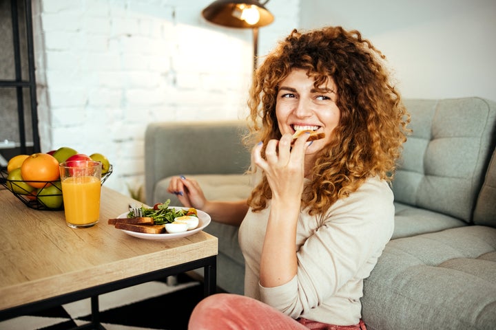 Woman is sitting on the floor in the living room and eating breakfast