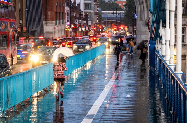 London, UK - Pedestrians on Tower Bridge at night in central London using umbrellas to shelter from the rain.