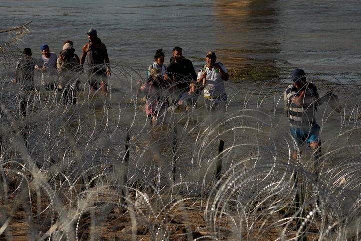 Migrants walk in the Rio Grande along a wall of concertina wire as they try to cross into the U.S. from Mexico on Friday in Eagle Pass, Texas.