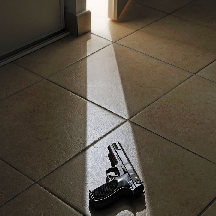 Ray of light spills on floor and handgun from partially open door