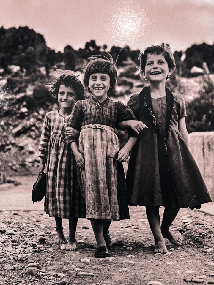 Η Λαμπρινή, η Μαρία κι η Ελένη: μικρά κορίτσια στέκονται χαμογελαστά μπροστά στον φακό του καλλιτέχνη σε ηπειρώτικη γέφυρα σε μια από τις πιο εμβληματικές φωτογραφίες του οδοιπορικού του στην μεταπολεμική Ελλάδα. 