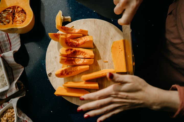 Caucasian woman slicing a Butternut Squash on a wooden cutting board. High view