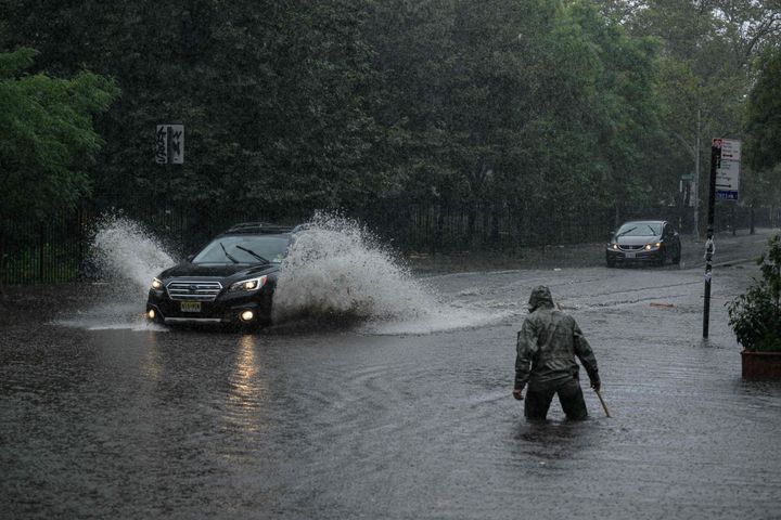 A man clears debris from a drain as a car make their way through floodwater in Brooklyn, New York on September 29, 2023. (Photo by Ed JONES / AFP) (Photo by ED JONES/AFP via Getty Images)