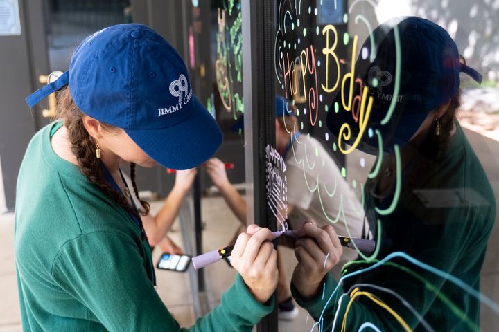 Courtney Lonsway, a volunteer at The Carter Center in Atlanta, writes birthday wishes on the center's window during a celebration for former President Jimmy Carter's 99th birthday held on Saturday. (AP Photo/Ben Gray)