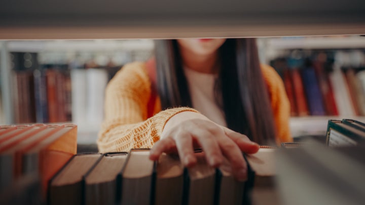 Close-up of a teenage girl choosing a book from the shelf in a library.