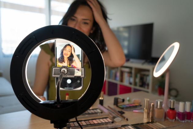 woman recording a makeup tutorial for her beauty blog with her phone while sitting at home. female influencer live streaming her cosmetic review and recommendation online