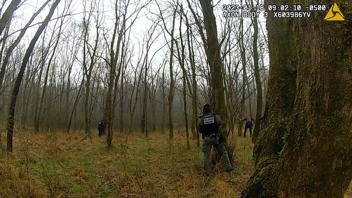 In this image taken from body cam video released by the Atlanta Department, officers stand behind trees after hearing gunfire near the future site of City of Atlanta’s Public Safety Training Center on Jan. 18, 2023, near Atlanta, Georgia. Authorities said Manuel Esteban Paez Teran, an environmental activist who went by the name Tortuguita, died at the scene, and a state trooper was injured with a gunshot wound.