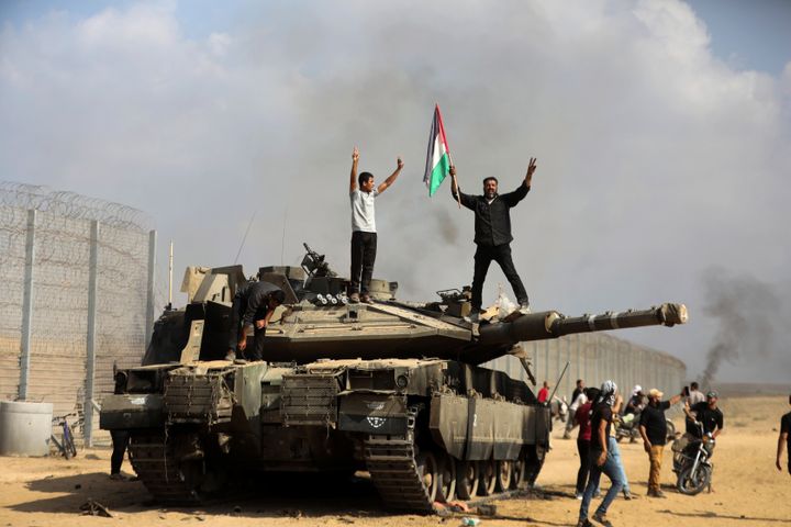 Palestinians wave their national flag and celebrate by a destroyed Israeli tank at the Gaza Strip fence east of Khan Younis southern Saturday, Oct. 7, 2023. The militant Hamas rulers of the Gaza Strip carried out an unprecedented, multi-front attack on Israel at daybreak Saturday, firing thousands of rockets as dozens of Hamas fighters infiltrated the heavily fortified border in several locations by air, land, and sea and catching the country off-guard on a major holiday. (AP Photo/Yousef Masoud)