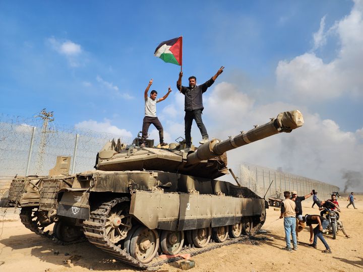 破壊したイスラエル軍の戦車の上に立ち、パレスチナの旗を振るハマスの武装組織＝2023年10月7日、ガザ地区