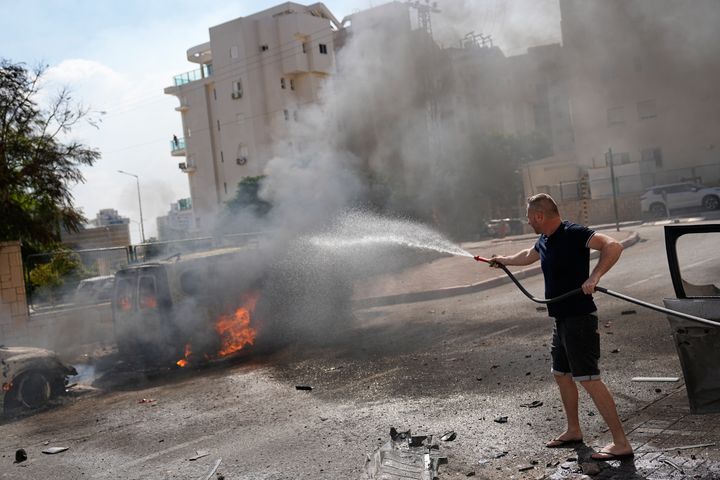 パレスチナ武装勢力からのロケット弾で炎上した車。イスラエル市民とみられる人が消火活動をしている。（10月7日）