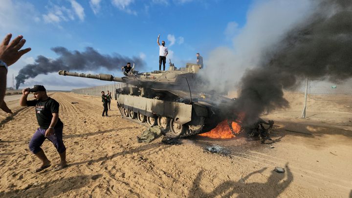 Palestinians celebrate by a destroyed Israeli tank at the Gaza Strip fence east of Khan Younis on Saturday, Oct. 7, 2023.