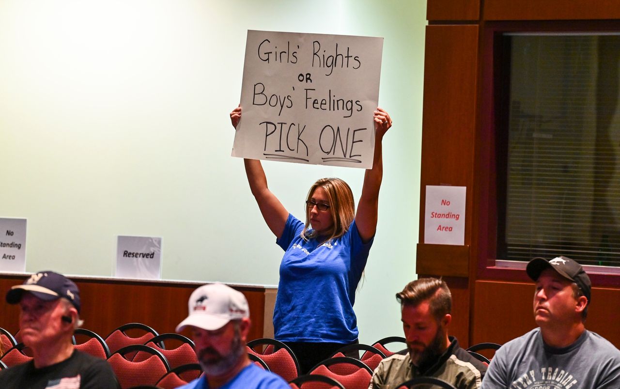 A woman holds a sign as Loudoun County school board members vote to enact Policy 8040 during a school board meeting on Aug. 11, 2021, in Ashburn. 