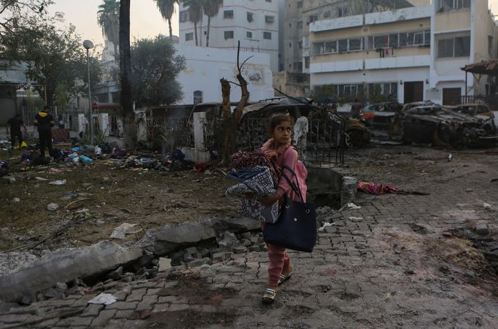 A Palestinian girl carries a blankets as she walks past the explosion science at al-Ahli hospital, in Gaza City, Wednesday, Oct. 18, 2023.