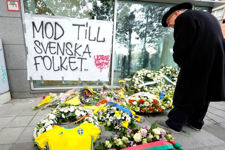 Στο πεζοδρόμιο τοποθετούνται λουλούδια, μια φανέλα της σουηδικής ομάδας και συλλυπητήρια σημειώματα, ενώ μια πινακίδα γράφει "κουράγιο στον σουηδικό λαό" κατά τη διάρκεια εκδήλωσης μνήμης για τα θύματα των πυροβολισμών στο κέντρο των Βρυξελλών, Τετάρτη 18 Οκτωβρίου 2023.