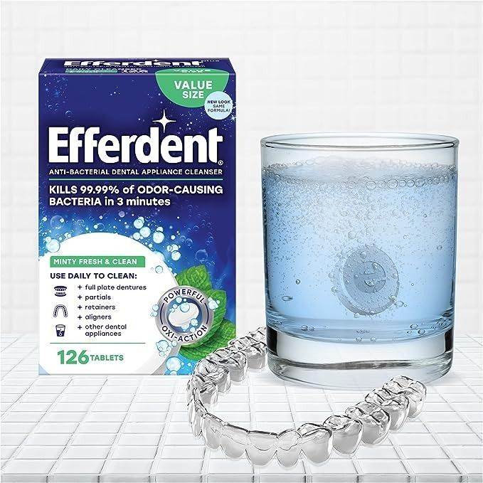 A box of Efferdent cleaning tablets next to one of the tablets fizzling in a cup and a mouthguard.
