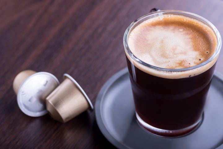 Black glass coffee espresso cup with two pods on wooden table.