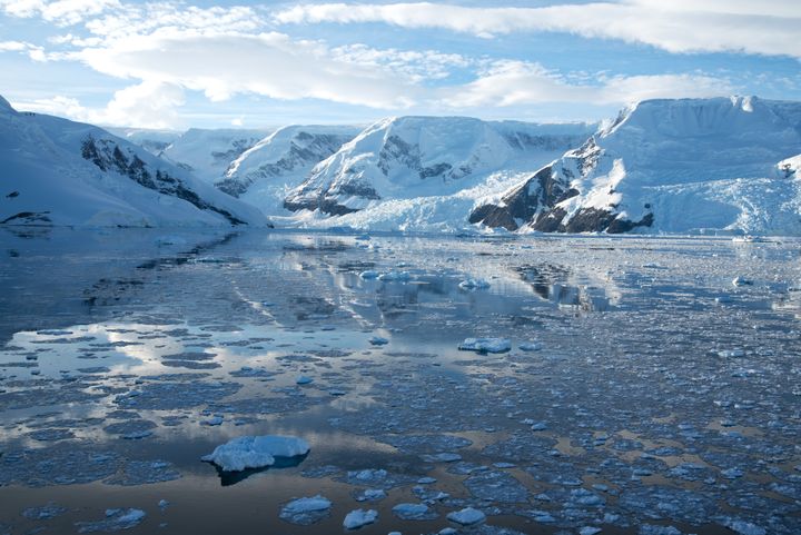 Mountains and glaciers are reflected in ice strewn waters of an Antarctic Peninsula channel.