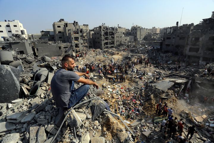 A man sits on the rubble as others wander among debris of buildings that were targeted by Israeli airstrikes in Jabaliya refugee camp, northern Gaza Strip, Wednesday, Nov. 1, 2023. (AP Photo/Abed Khaled)