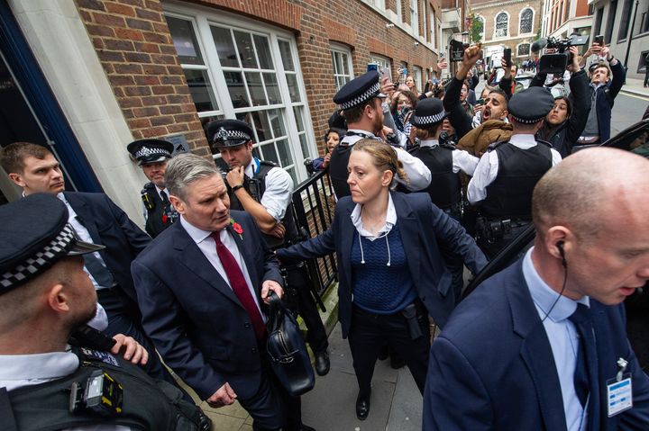 Keir Starmer is surrounded by Police as he leaves Chatham House in London after delivering a speech on the situation in the Middle East, while demonstrators protest outside.