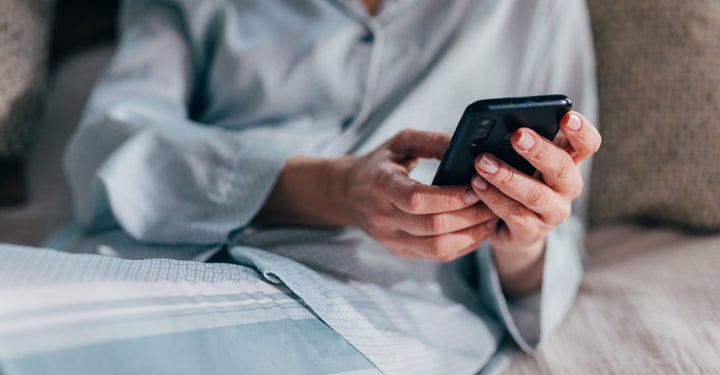 A woman texts on her phone while lying in bed.