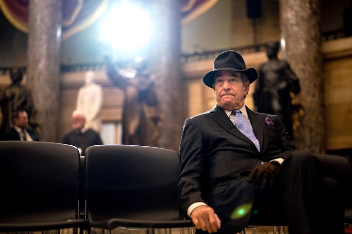 Paul Pelosi sits following a portrait unveiling ceremony for his wife in December 2022, wearing a hat and a glove over his left hand.