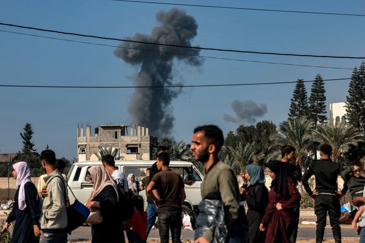 Smoke from Israeli bombardment rises behind people fleeing Gaza City and other parts of the northern Gaza Strip towards the south of the Palestinian enclave as they walk along a highway on November 9, 2023