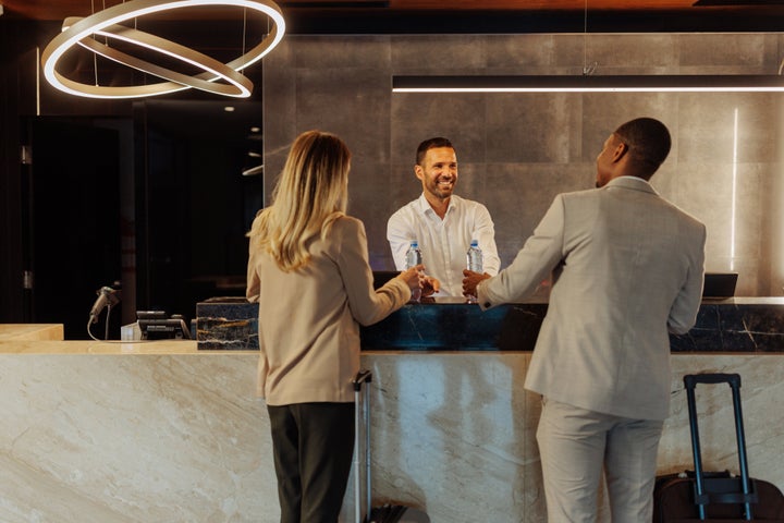 Diverse couple standing by hotel reception, booking a room and getting water bottles