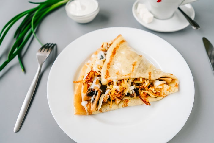 Person eating crepes with filling. Tasty breakfast on gray background. Front view.