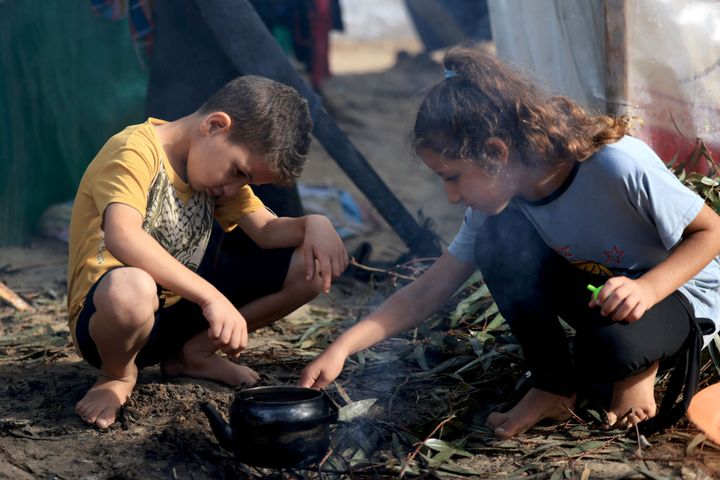 Displaced Palestinian children, who fled from the Israeli bombardment of the northern Gaza Strip and are now living in makeshift shelters, light a fire to boil a kettle after overnight rainstorms in Khan Yunis, on November 15, 2023.