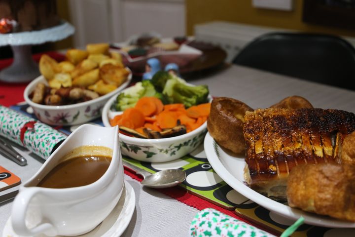 Roast dinner including pork crackling joint and dishes of vegetables and gravy.