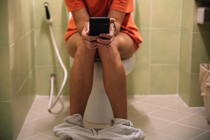 Woman sitting on a toilet holding a mobile phone in her hands